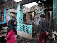 Kashmiri people assess the damaged residential house where three militants were killed in a military operation in Newa area of Pulwama distr...