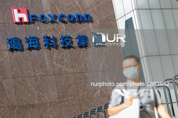 A man with a face mask walks past the  logo of Foxconn, or Hon Hai Group , which is Taiwan’s technology giant and the world’s leading produc...
