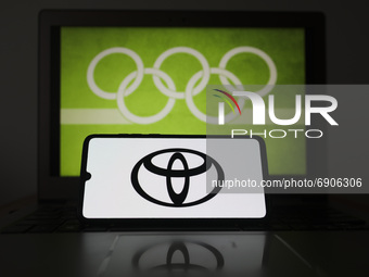 Toyota logo is displayed on a mobile phone screen photographed with Olympic rings symbol on the background for illustration photo. Leszczewe...