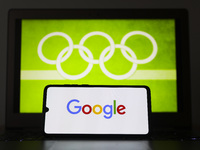 Google  logo is displayed on a mobile phone screen photographed with Olympic rings symbol on the background for illustration photo. Leszczew...