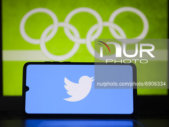 Twitter logo is displayed on a mobile phone screen photographed with Olympic rings symbol on the background for illustration photo. Leszczew...