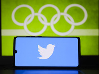 Twitter logo is displayed on a mobile phone screen photographed with Olympic rings symbol on the background for illustration photo. Leszczew...