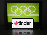 Tinder logo is displayed on a mobile phone screen photographed with Olympic rings symbol on the background for illustration photo. Leszczewe...