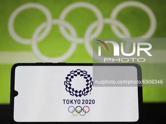 Tokyo Olympics 2020 logo is displayed on a mobile phone screen photographed with Olympic rings symbol on the background for illustration pho...