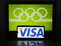 VISA card logo is displayed on a mobile phone screen photographed with Olympic rings symbol on the background for illustration photo. Leszcz...
