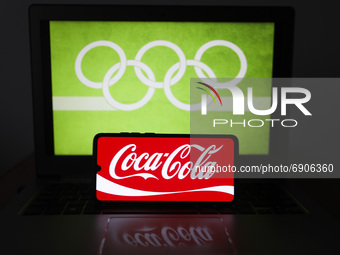  Coca-Cola logo is displayed on a mobile phone screen photographed with Olympic rings symbol on the background for illustration photo. Leszc...