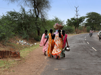 Group of Indian women carry baskets with tools on their heads as they walk along the roadside in Chandrapur, Maharashtra, India, on June 18,...