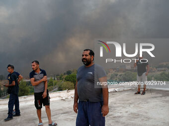 Local residents and migrant workers look on as a forest fire rages in Varybobi, north of Athens, on August 3, 2021. Residential areas in Ath...