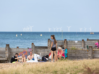 Holidaymakers enjoy sunny summer day at the beach in Whitstable, south-eastern coastal town of England with Kentish Flats windmills power pl...