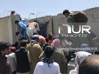 People struggle to cross the boundary wall of Hamid Karzai International Airport to flee the country after rumors that foreign countries are...