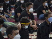 An Afghan refugee young boy wearing a protective face mask wears a religious headband while attending with his father at a Muharram mourning...