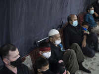 An Afghan refugee young boy wearing a protective face mask and a religious headband looks on while attending a Muharram mourning ceremony fo...