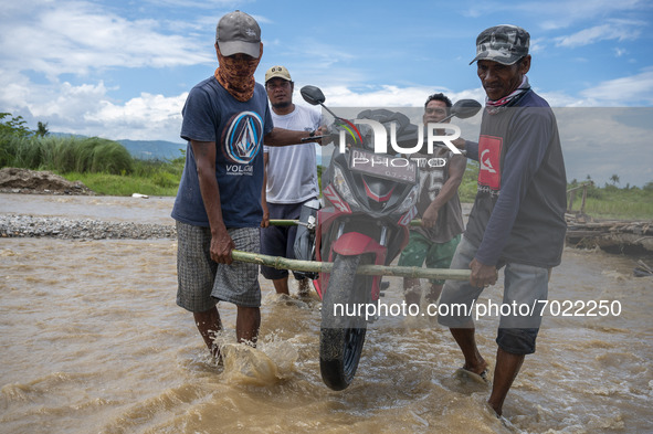 Residents lift motorbikes across a road covered with overflowing river water in Jono Oge Village, Sigi Regency, Central Sulawesi Province, I...