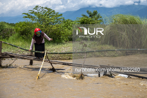 A woman tries to cross an emergency bridge footbridge to avoid overflowing river water that has blocked a road in Jono Oge Village, Sigi Reg...