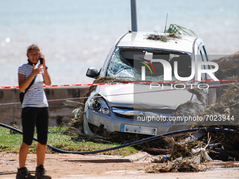 A woman speaking on the phone in front of a car damaged by floods on street filled with mud and derbis the day after flash floods on Septemb...