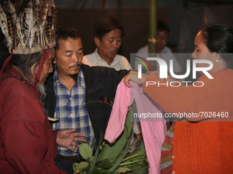 A 90 year-old Lepcha Bomthing (Lepcha priest) wearing a feathered hat chants prayers and uses leaves to bless the sweater of a village girl...