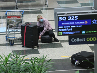 A female passenger wearing protective mask collects her bags after arriving on flight SQ 325 from Frankfurt at Changi International Airport...