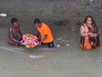 Devotees carry an idol of Ganesh for immersion as a lady prays standing in water , at a Ganges riverside in Kolkata , India , on 12 Septembe...