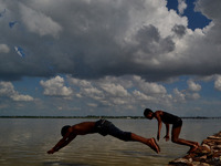 Indian boys jump to take bath in flooded River Ganges as patchy clouds loom overhead  in Allahabad on July 26,2015.Water level of River Gang...