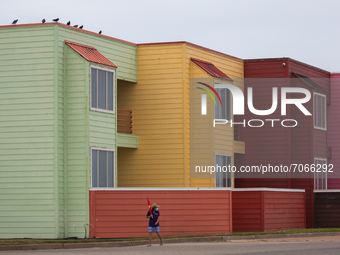 A masked woman with an umbrella walks past a row of beach houses in Galveston, Texas, on September 12th, 2021, as Tropical Storm Nicholas ap...