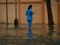 A woman holds a mobile phone while walking through a water-logged road during a heavy rain in Bangkok on September 19, 2021 in Bangkok, Thai...