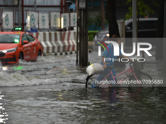 A woman is seen wearing a face mask pushes her bicycle through a water-logged road during a heavy rain in Bangkok on September 19, 2021 in B...