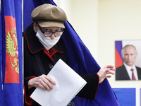 A woman at a polling station walks past a portrait of Russian President Vladimir Putin during a vote in the State Duma of the Russian Federa...