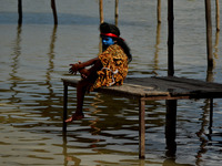 An indian boy,dressed as hindu God Shiva,sit on a table beside a road,filled with water of floooded Ganes River as he waits for a rescue boa...