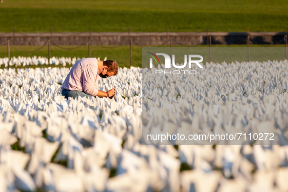 A person kneels to take photos of some of the more than 670,000 white flags covering 20 acres of the National Mall in an art memorial for Co...