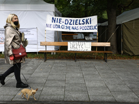 A woman with a small dog walks past a banner reading 