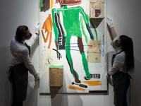 LONDON, UNITED KINGDOM - OCTOBER 08, 2021: Staff members adjust a painting by Jean-Michel Basquiat (1960-1988) 'Because it Hurts the Lungs',...