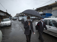 Two Iranian men wearing protective face masks walk along a street next to a local bazaar located on a riverside in the seaport city of Anzal...