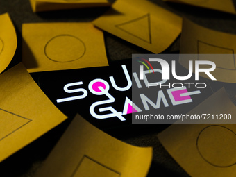 Squid Game series logo displayed on a phone screen and symbols known from the series, drawn on pieces of paper, are seen in this illustratio...