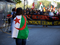 A woman wrapped in an algerian flag films the protest. The banner reads 'October 17th 1961 a state colonialist slaughter'. Dozens of protest...