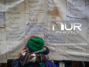 Two women are seen hugging in front of a sign with the names of refugees caugth crossing the border from Belarus into Poland during a rally...