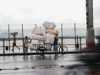 Indian Laborers push a cycle van loaded vegetable cover the plastic protects rain across the Howrah Bridge during heavy rainfall in Kolkata,...