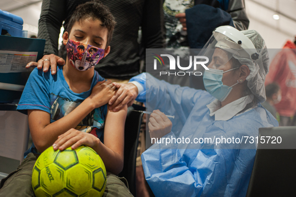 A children receives a dose of the COVID-19 vaccine as he holds a football as the Colombian government begins to vaccinate children between a...