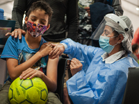 A children receives a dose of the COVID-19 vaccine as he holds a football as the Colombian government begins to vaccinate children between a...
