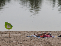 A woman is sunbathing on Verbne lake shore next to the caution “Swimming is temporarily prohibited” board with kids swimming circle hung on....