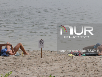 A men sunbathe on Verbne lake shore next to the caution “Swimming is temporarily prohibited” board. Several people were deadly infected with...