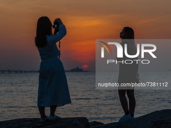 Two young ladies take pictures of themselves in front of the sunset near Hong Kong International Airport. (