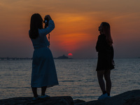 Two young ladies take pictures of themselves in front of the sunset near Hong Kong International Airport. (