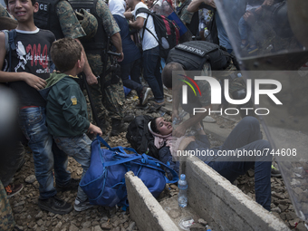 A young migrant woman faints after waiting on the Macedonian-Greek border where migrants are being held, since Macedonia declared emergency...