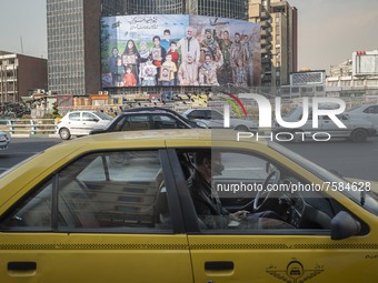 An Iranian yellow cab driver sits at his vehicle which is parked on a corner of a square in downtown Tehran on December 30, 2021, as a giant...