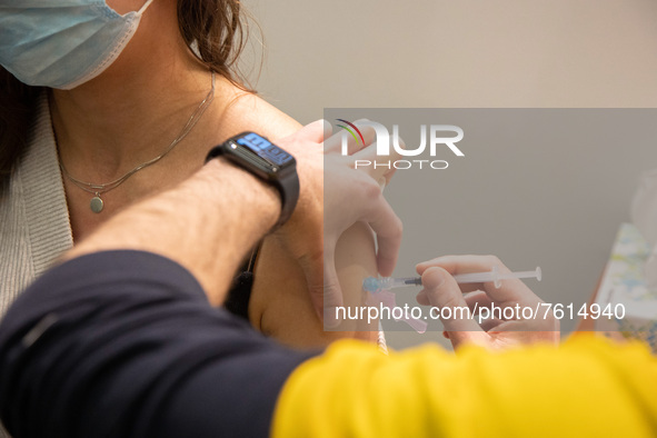 Close up at the syringe during the vaccination. A young woman wearing facemask is getting the Covid shot vaccine by a medical health care wo...