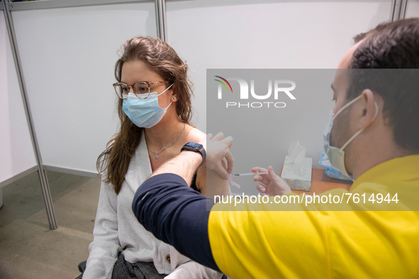 A young woman wearing facemask is getting the Covid shot vaccine by a medical health care worker in the vaccine booth pod. Vaccination cente...
