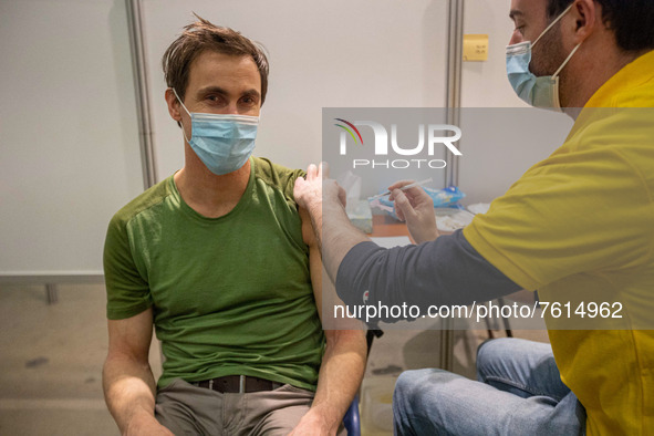 A man wearing facemask is getting the Covid shot vaccine by a medical health care worker in the vaccine booth pod. Vaccination center in Ein...