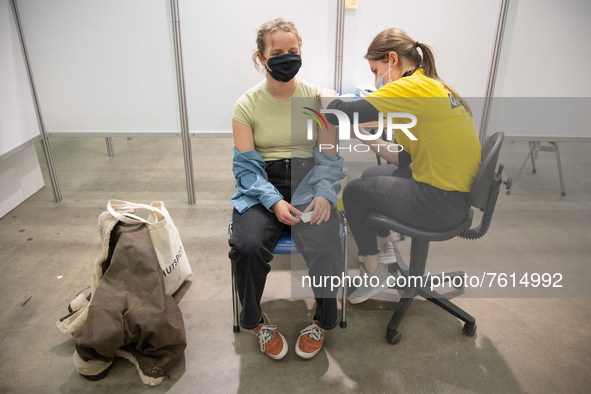 A young woman wearing facemask is getting the Covid shot vaccine by a medical health care worker in the vaccine booth pod. Vaccination cente...