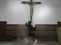 A worker sanitises an image of a crucified Christ on a wall inside the Cathedral of San Bernardino de Siena in Xochimilco, Mexico City, foll...