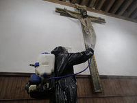 A worker sanitises an image of a crucified Christ on a wall inside the Cathedral of San Bernardino de Siena in Xochimilco, Mexico City, foll...